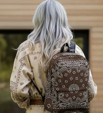 Load image into Gallery viewer, Melodia Gallery brown bandana print backpack with white paisley design, featuring a front zip pocket and padded straps.