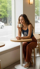 Load image into Gallery viewer, Melodia Gallery navy blue 100% cotton micro rib crop tank with lotus bloom graphic. Model sits at a cafe table.