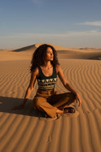 Load image into Gallery viewer, Melodia Gallery dark green cotton crop top with Egyptian lotus pattern, worn by a woman sitting in the desert.
