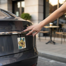 Load image into Gallery viewer, Melodia Gallery yellow hibiscus flower car magnet with green leaves on a cream background.
