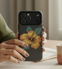 Load image into Gallery viewer, Melodia Gallery dark grey iPhone case with yellow hibiscus flower and green leaves design. MagSafe compatible.
