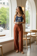 Load image into Gallery viewer, Melodia Gallery navy blue 100% cotton micro rib crop tank with vintage lotus bloom graphic. Model wears it with rust linen pants.
