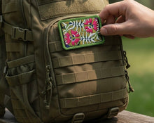 Load image into Gallery viewer, Melodia Gallery embroidered patch with pink passionflowers and green foliage on a tactical backpack.
