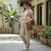 Load image into Gallery viewer, Melodia Gallery brown faux leather crossbody bag with phoenix and floral embossed design, worn by a woman.
