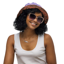 Load image into Gallery viewer, Melodia Gallery Phoenix + Flora reversible bucket hat with intricate earth-tone pattern and lavender/blue side. Model wears sunglasses.

